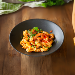 a bowl of pasta with shrimp and herbs on a wooden table